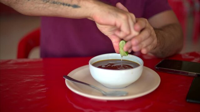 Slow motion of a latin man squeezing a lime into his broth stock soup in a mexican restaurant on a red table