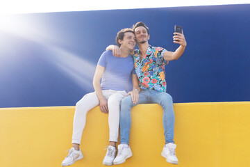 Happy young couple embraces. Two men taking selfie photo outside.