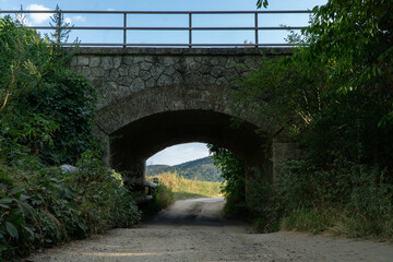 A tunnel under a train bridge with beautiful scenery in the background on a dirt road in slovakia