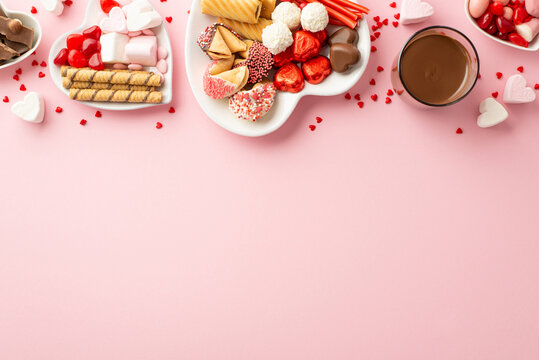 Valentine's Day celebration concept. Top view photo of glass of drinking heart shaped plates with sweets cookies chocolate and jelly candies on isolated pastel pink background with copyspace