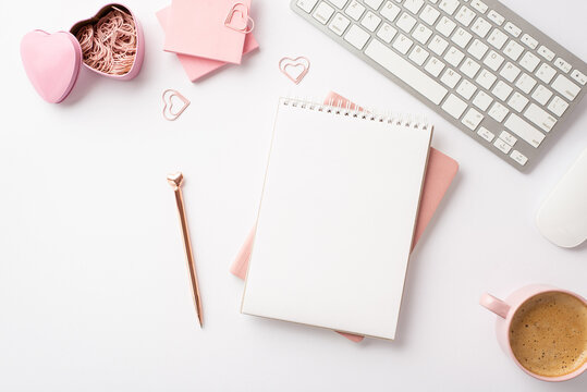 Valentine's Day concept. Top view photo of workspace planners pen keyboard pink sticky note paper heart shaped clips holder and cup of coffee on isolated white background with blank space