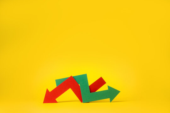 Indecision in the stock or crypto market. Red and green arrows intertwined on yellow background. Economic growth or global recession.