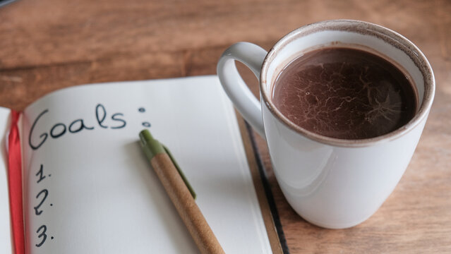 Taza de chocolate caliente con una libreta de planificaci&oacute;n de logros
