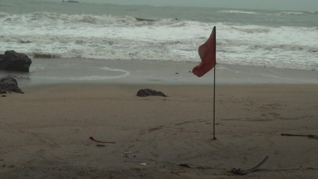 Red flag on thin stick stuck in the sand on a beach in winter with waves in the background
