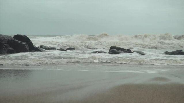Waves rolling over and crashing on a rocky coastline and pulling back sand as water flows back to sea