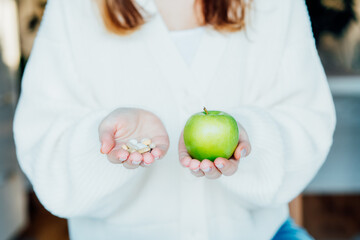 Female hands with green apple and different pills. Choose between natural, folk and traditional...