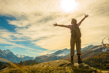 Woman with Rucksack Hiking in the Mountain with Arms Outstretched with Sunlight in San Bernardino, Grisons, Switzerland.