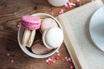 Macaroons in a bowl, a cup of coffee, on a background of small hearts on a wooden background