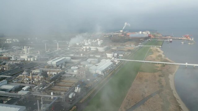 Smoke and steam rising of an industrial facility on a river, CO2 emissions, air pollution, exhaust gases, aerial, flight through steam