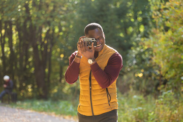 African american guy photographer taking picture with vintage camera on city green park copy space - leisure activity, diversity and hobby concept