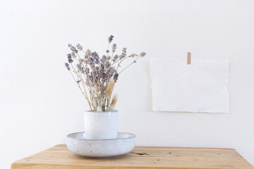 Modern ceramic vase with Lavender flowers, on a vintage bench, table, and blank paper on the wall background. Scandinavian interior.
