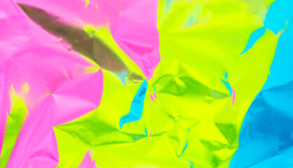 The surface of the crumpled foil is highlighted in different colors. Background holographic iridescent multicolored texture.