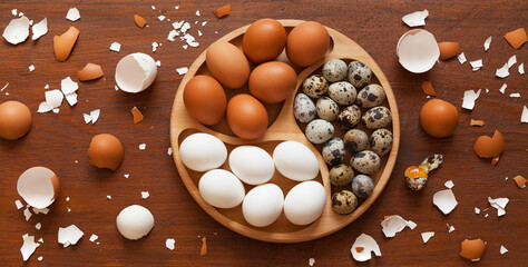 Flat lay of chicken eggs with white and brown shells and spotted quail eggs on a wooden table. Dietary organic farm food. Top view, close up,  mockup