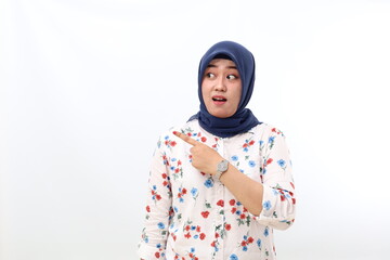 Surprised asian veiled woman standing while pointing sideways. Isolated on white background with copyspace