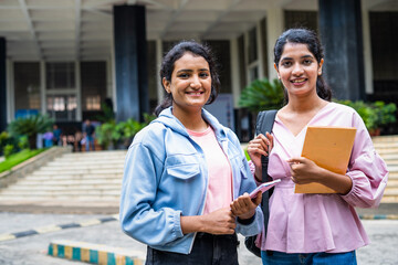 Happy smiling students standing by holding books while looking camera at college campus - concept...