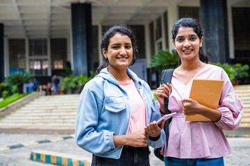 Happy smiling students standing by holding books while looking camera at college campus - concept of knowledge, friendship and learning.