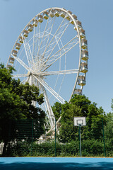 Fototapeta premium a Ferris wheel on a sunny day in front of a basketball court with a hoop and a blue base in Budapest