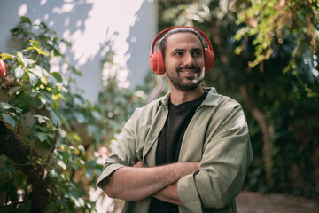 Portrait of a young man in bright large headphones in green foliage.