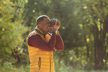 Close-up african american guy photographer taking picture with photo camera on city green park copy...