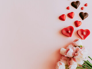 Pink blossoming ranunculus on pink festive background, red candles, gift, chocolate and hearts confetti.