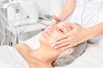 Cosmetologist rubbing moisturizing cream mask into woman face skin for rejuvenation, anti aging...