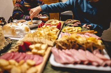 Hand of guy dipping crackers on soy sauce with cream cheese, a wooden board with salami, crackers, charcuterie, variety of cheeses, ham, nuts and a cake