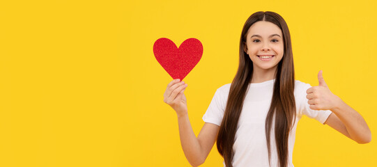 Fototapeta na wymiar happy kid hold love heart show thumb up on yellow background. Kid girl portrait with heart love symbol, horizontal poster. Banner header with copy space.