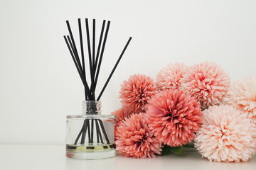 Composition with incense sticks, essential oil in a glass vase and pink terry artificial flowers in...