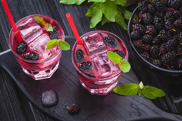 mulberry cocktail with ice and fresh mint on a black wooden table