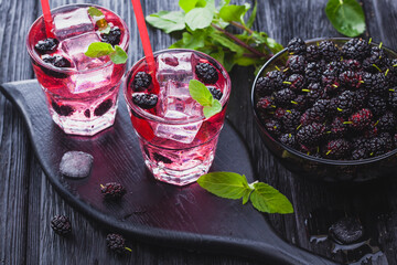 mulberry cocktail with ice and fresh mint on a black wooden table