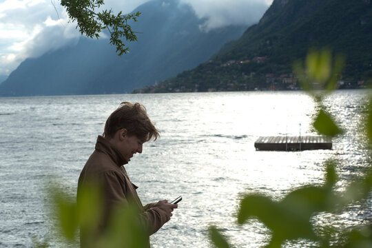 Young man sends text by lake edge and dock