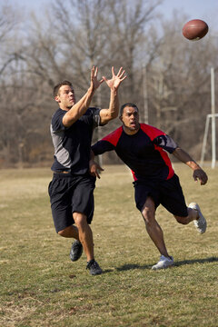 Two men in their twenties playing touch football competeing for pass.