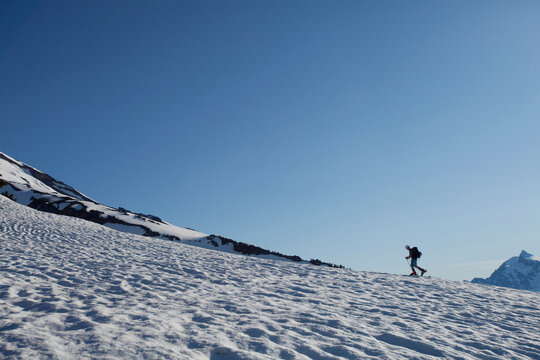 A lone skier skins up a snowy ridge at sunrise on a blue bird day.