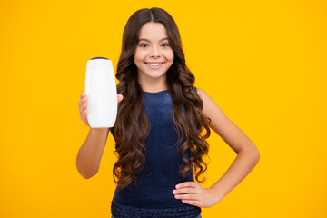 Teenager child girl showing bottle shampoo conditioners or shower gel isolated on yellow background. Hair cosmetic product. Mock up bottle. Happy girl face, positive and smiling emotions.