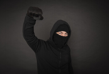 Man in the black hoody with hood wearing balaclava mask with fist up
