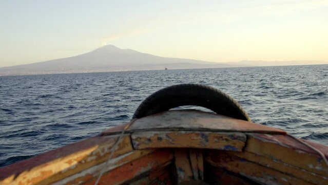 small boat on the sea in sicily in italy facing etna volcano smoking at sunrise