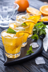 orange cocktail with ice and fresh mint on a black wooden table