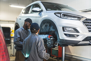 Two mechanics near a white luxury car on a lift in a car repair shop fixing tyres. High-quality...