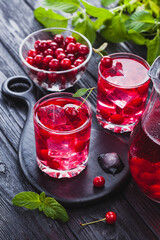 Red cherry cocktail with ice and fresh mint on a black wooden table