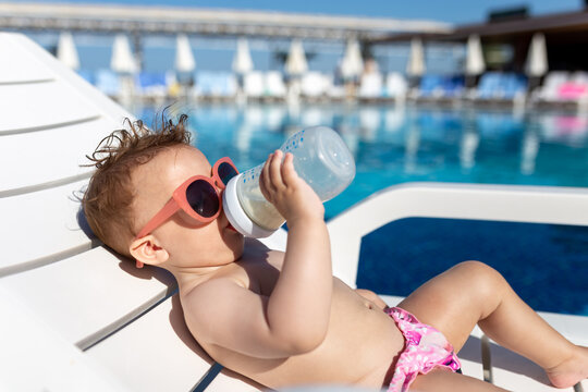 Portrait of fashionable baby drinking milk from the bottle and lying on lounger. Children and tourism concept.