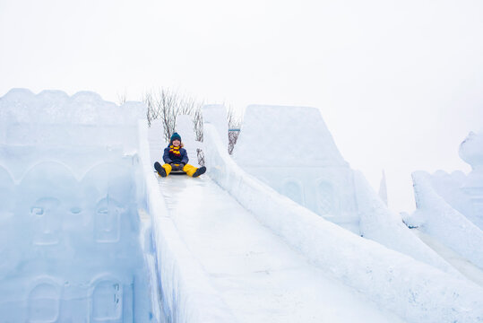 Happy Boy Slides Down An Ice Slide In Winter Outside