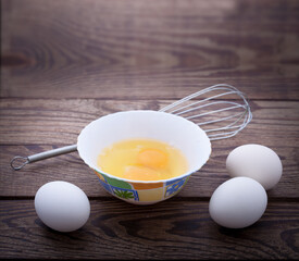 Raw eggs in bowl for whipping on wooden. Baking ingredients.