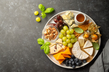 Cheese plate with various cheeses, fruits, nuts and snacks. Dark background.
