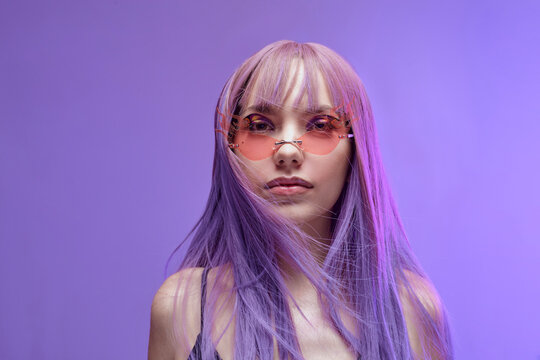 a beautiful stylish woman in a purple wig and fashionable glasses looks pleasantly at the camera
