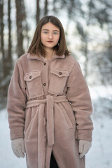 Portrait of a young beautiful long-haired girl in a gray fur coat made of artificial materials in a winter forest.