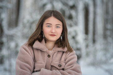 Portrait of a young beautiful long-haired girl in a gray fur coat made of artificial materials in a winter forest.