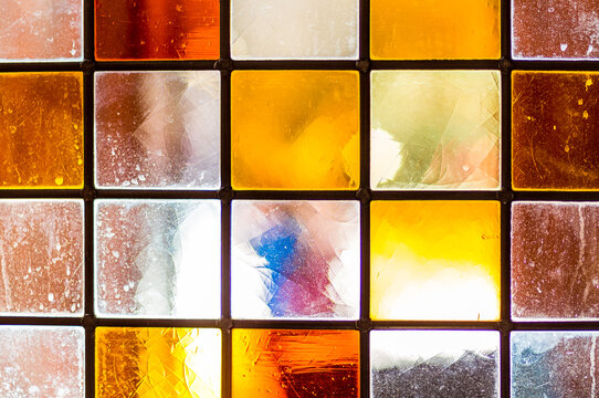 Lead-lined colourful chequered stained glass in Victorian pub window full of imperfections. Background.