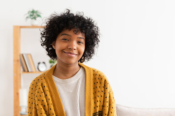 Beautiful african american girl with afro hairstyle smiling at home indoor. Young african woman with curly hair laughing in living room. Freedom happiness carefree happy people concept - obrazy, fototapety, plakaty