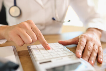 Female doctor counts price using calculator at her desk in medical clinic.