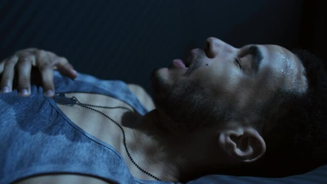 Side view close-up of young Black man sweating and having shortness of breath after nightmare getting up at night, PTSD concept